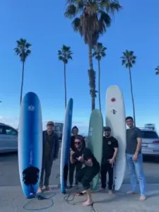 TJ Macklin posing with friends holding surf boards