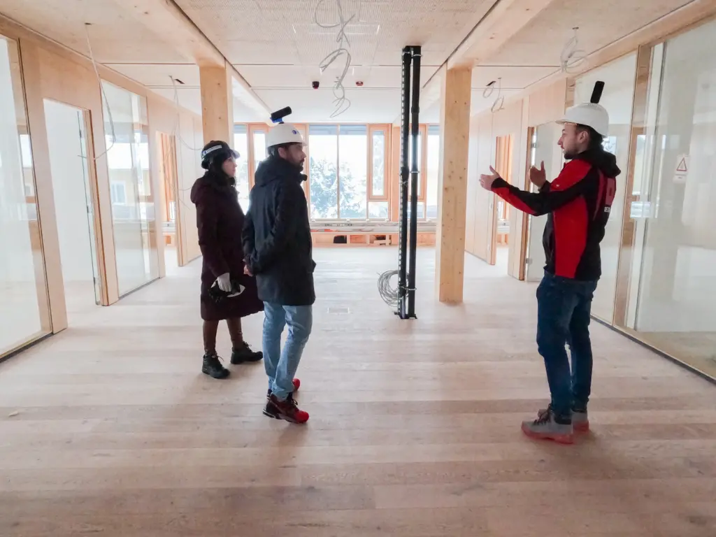 Three people on a construction side with a lot of wood elements. Two of them wear a helmet that has a 360 camera mounted on them